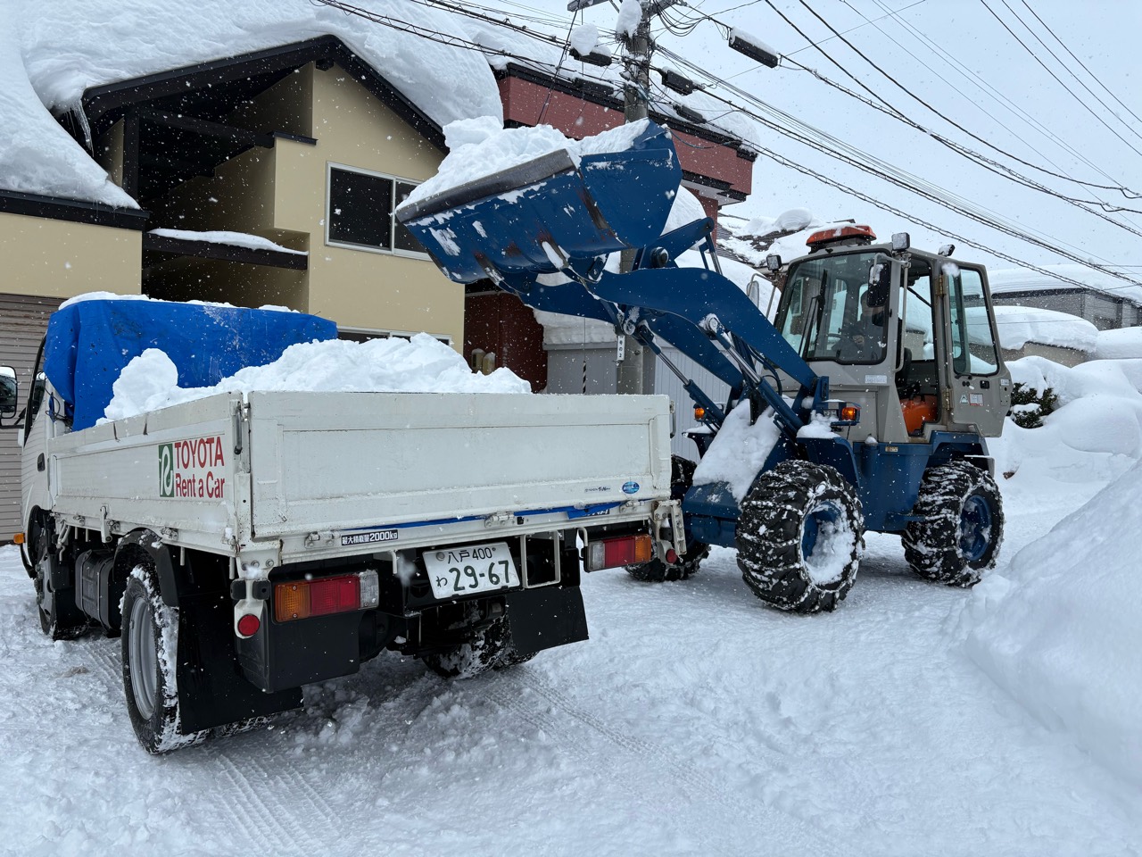 雪の積もった住宅地で、重機からトラックへ雪を積み込む様子