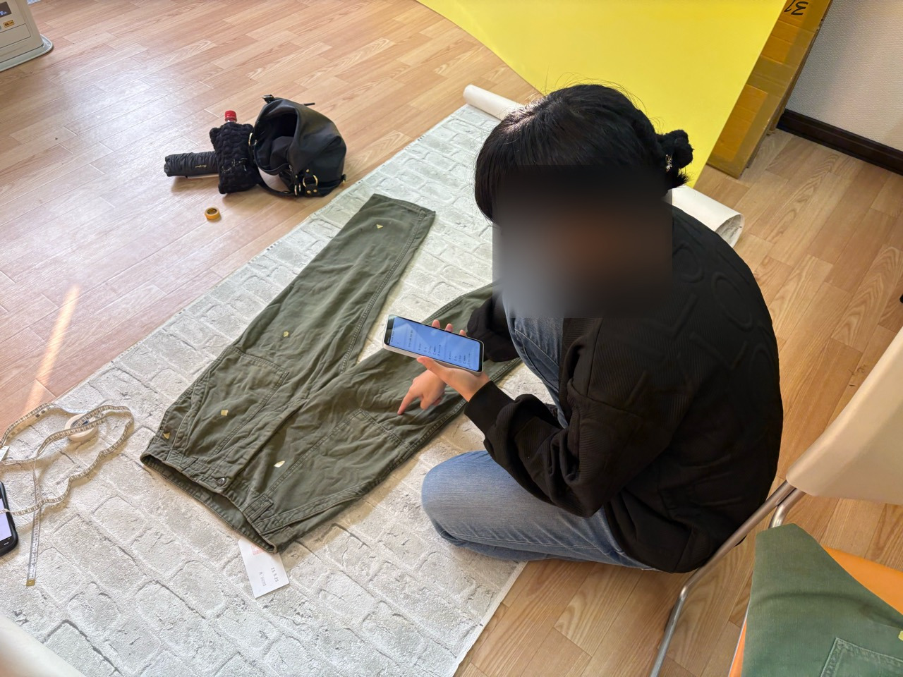広げたパンツのそばでスマートフォンを手に作業する様子